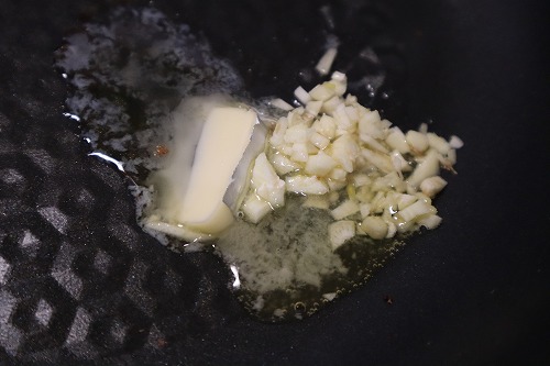 刻んだにんにくとバターをフライパンに入れて炒めているところ