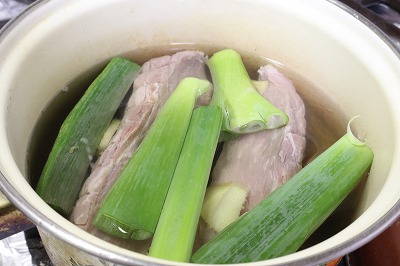 鍋に豚バラ肉とネギ、生姜を入れて煮ている調理過程